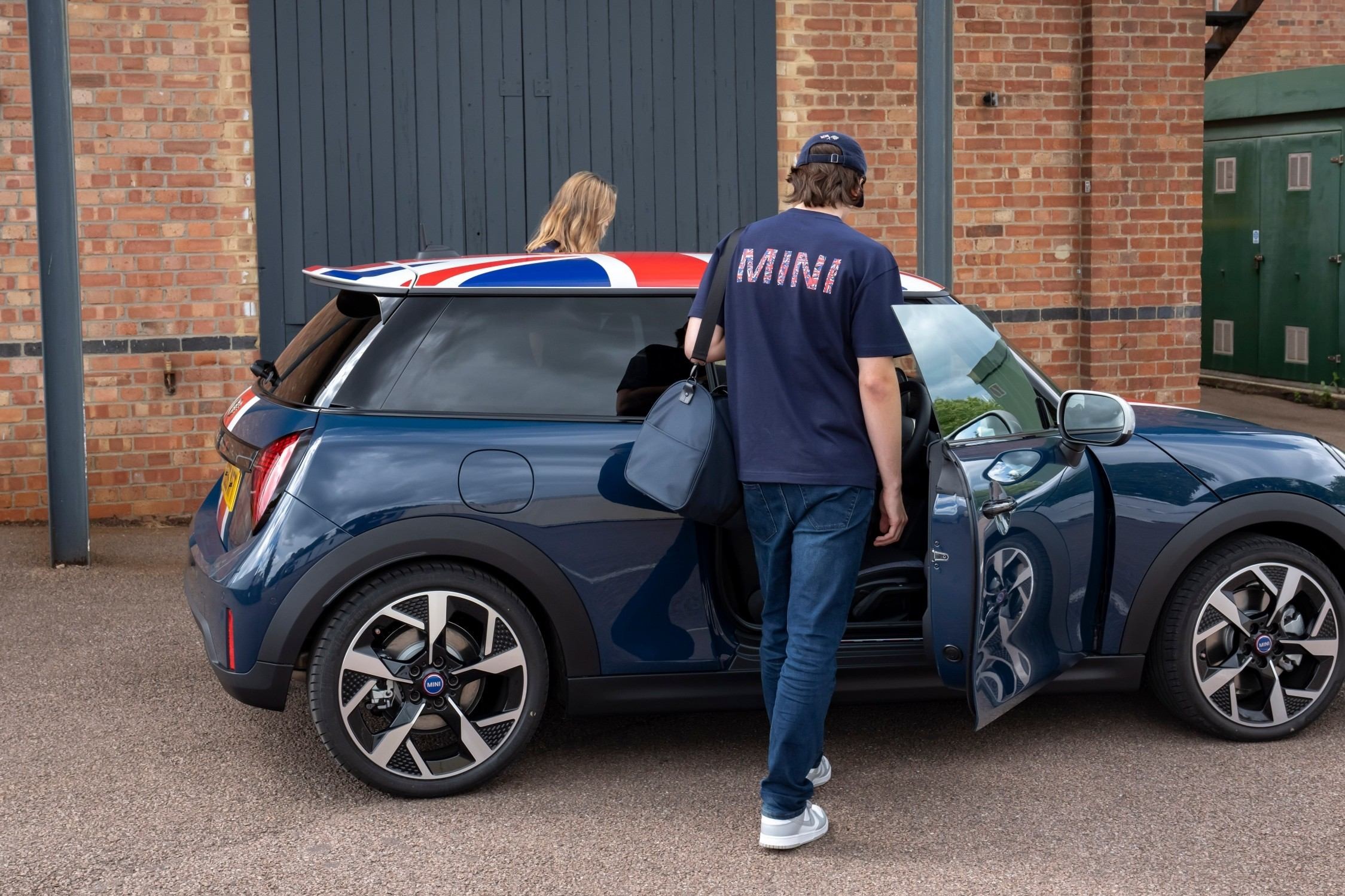 Duas pessoas junto ao MINI Cooper Oxford Edition azul, visto de perfil, com a porta aberta